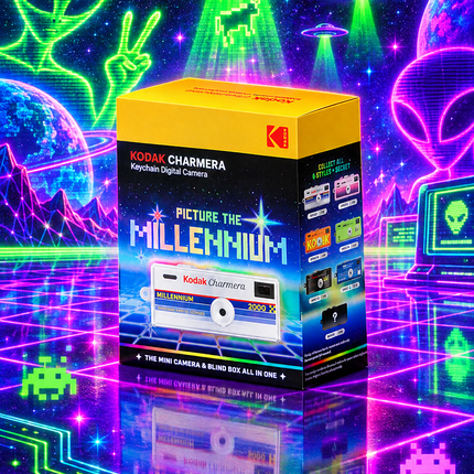 A boxed Kodak Charmont Keychain Digital Camera stands upright in a neon-lit sci-fi scene with glowing aliens, planets, and circuitry. The box is yellow, black, and blue, with the Kodak logo and product name clearly visible.